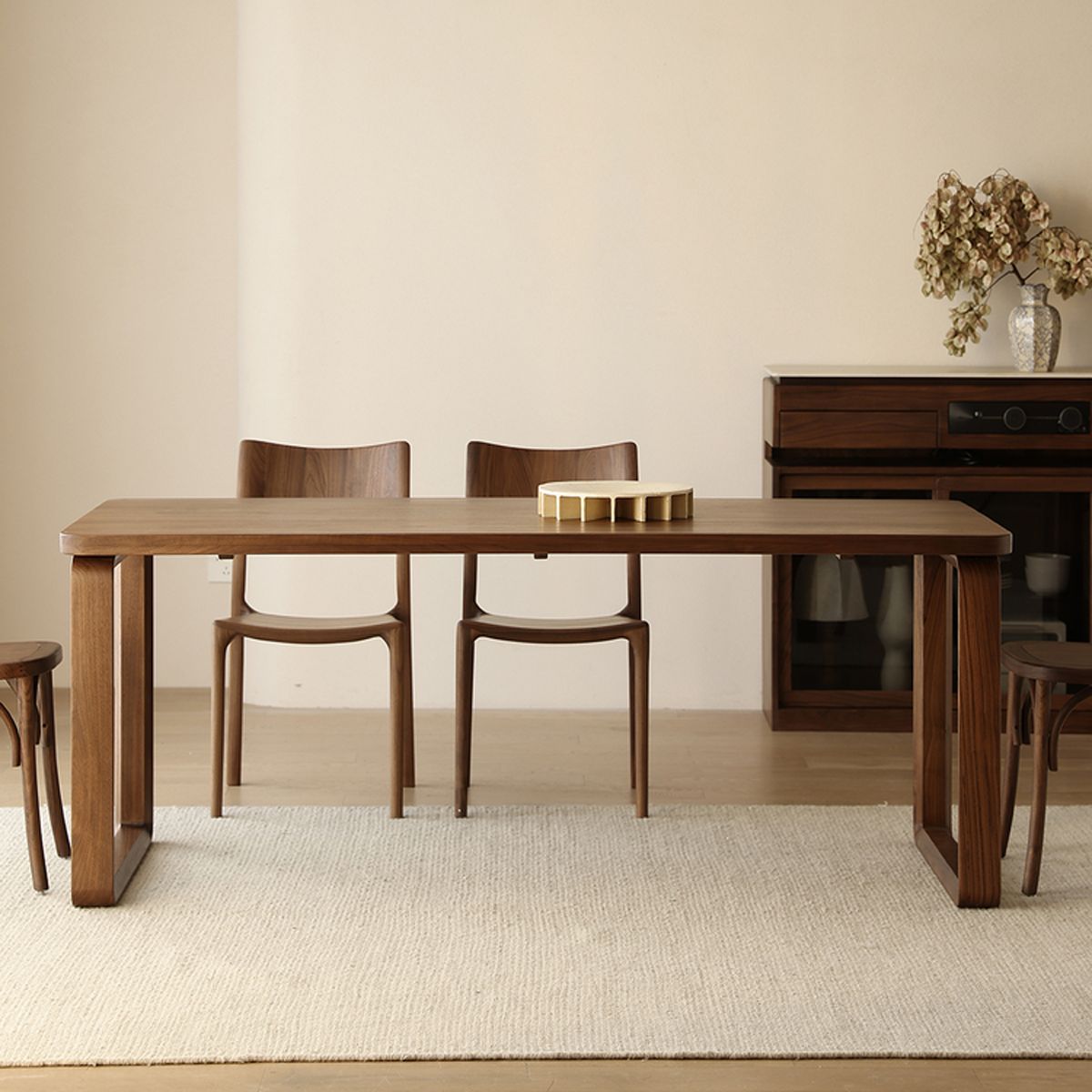 Minimalist dining room with wooden table, chairs, beige rug, and sideboard with dried flowers