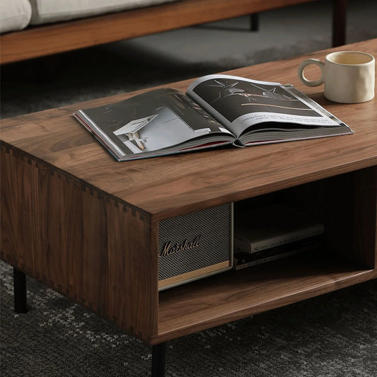 Solid black walnut coffee table with dovetail joints, open shelf holding a Marshall speaker and books, with a mug and open magazine on top