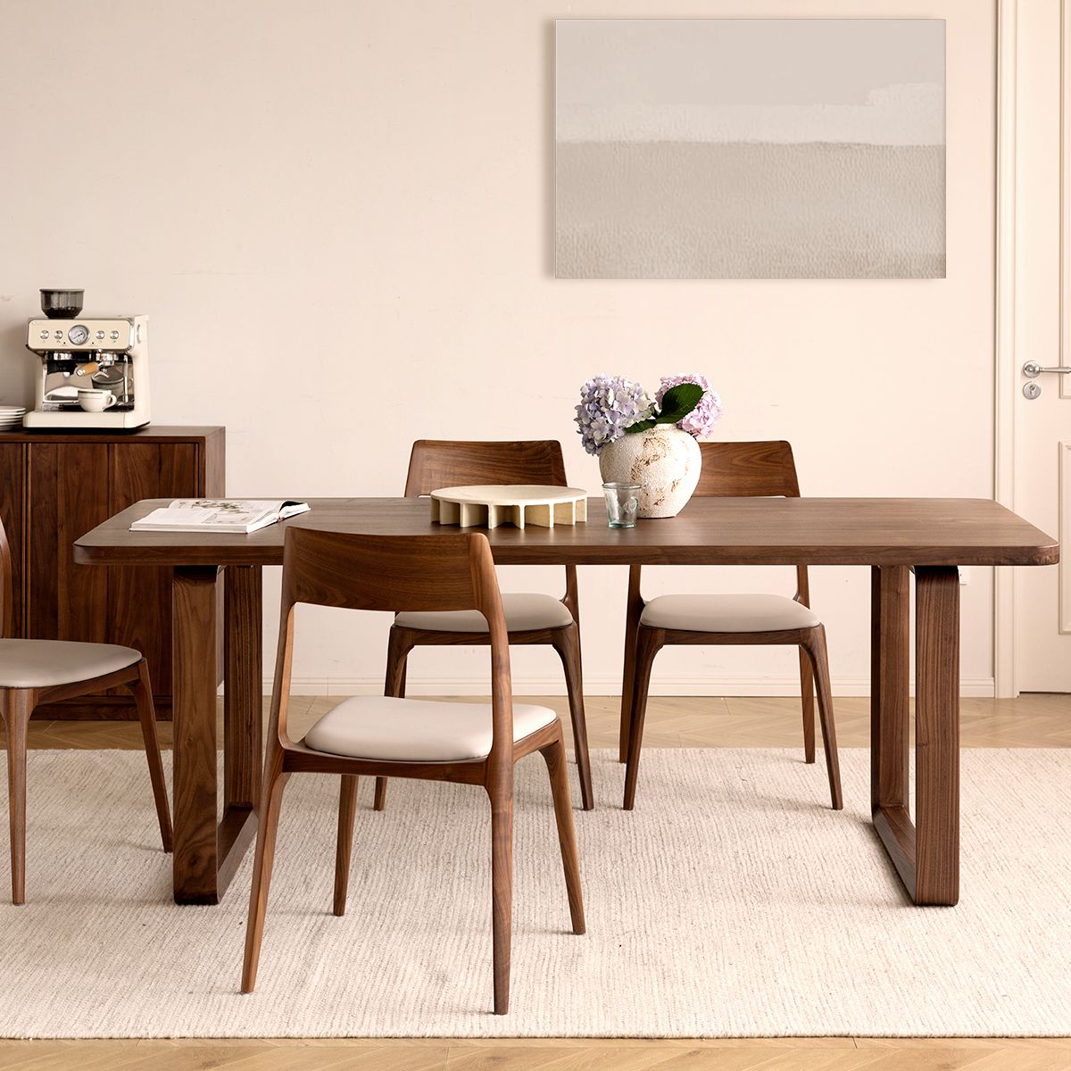 Modern dining room with wooden table and chairs, beige rug, abstract wall art, and coffee machine