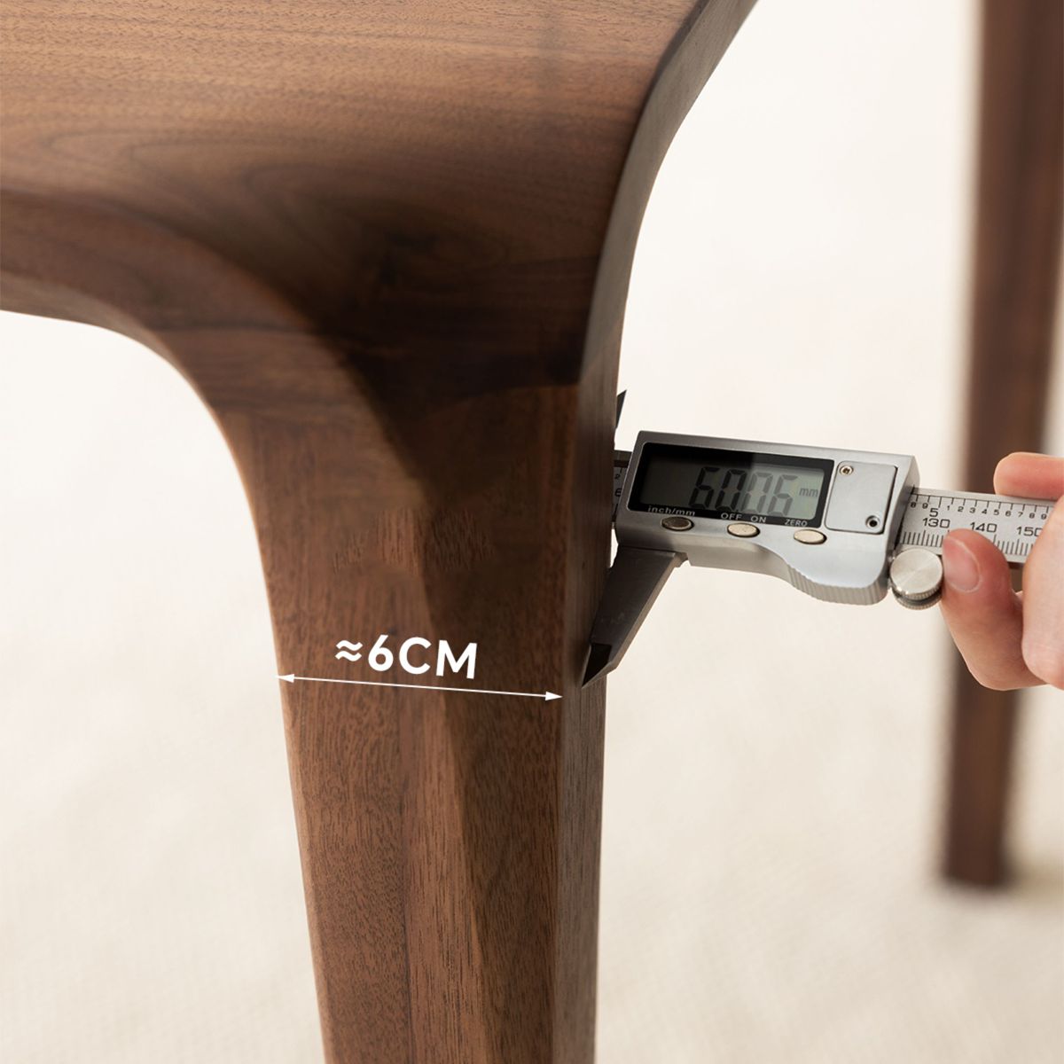 Digital caliper measuring 6cm thickness of smooth wooden chair leg in bright setting