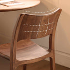 Curved ergonomic wooden chair with smooth grain backrest beside round wooden table in warm room