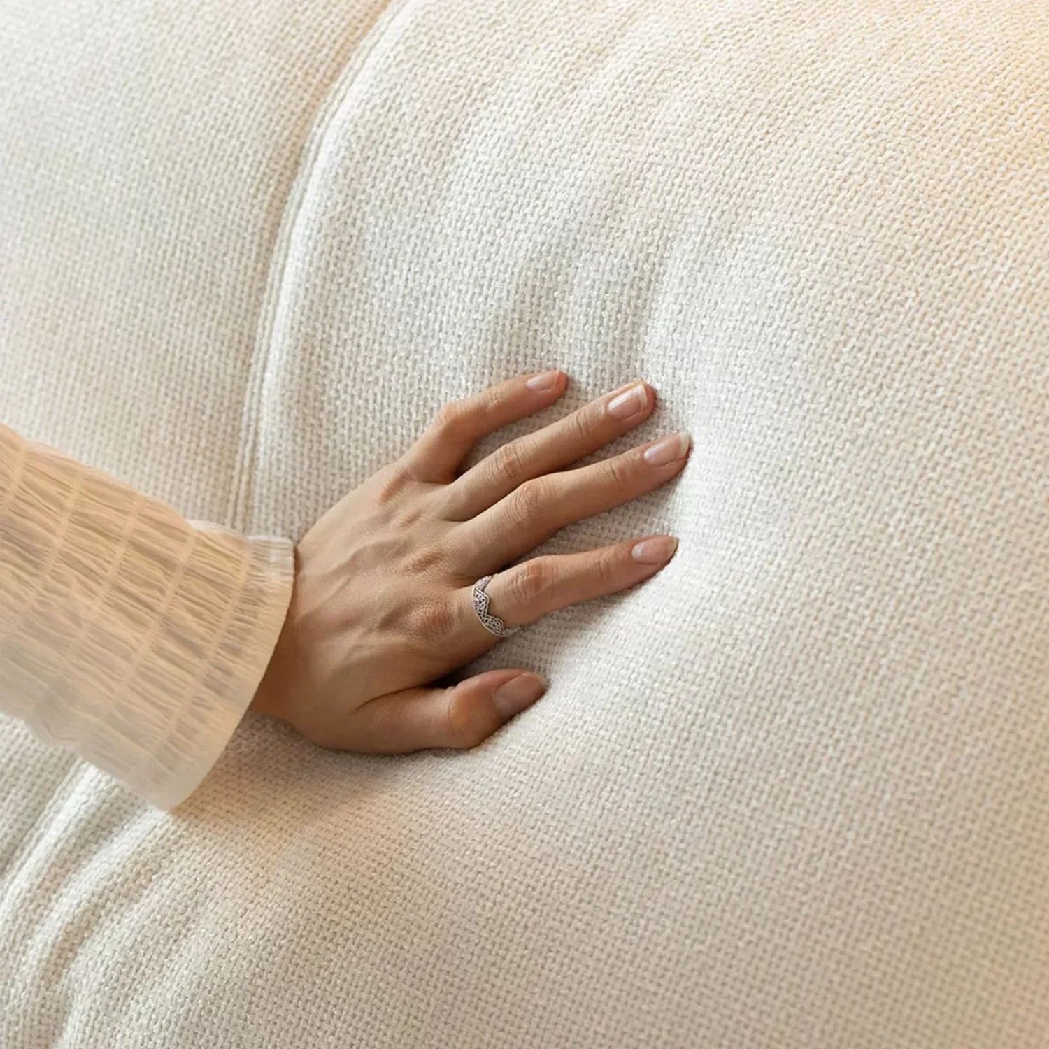 Hand pressing a soft, textured white down-filled cushion fabric, showing plush comfort detail