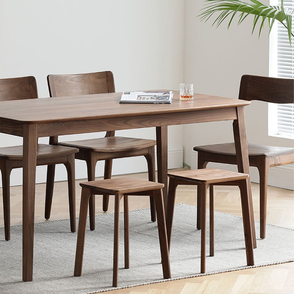 Modern wooden dining table with matching chairs and two stacking stools on a rug in a bright room