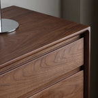 Close-up of walnut wood grain chest corner with smooth finish and metal lamp base