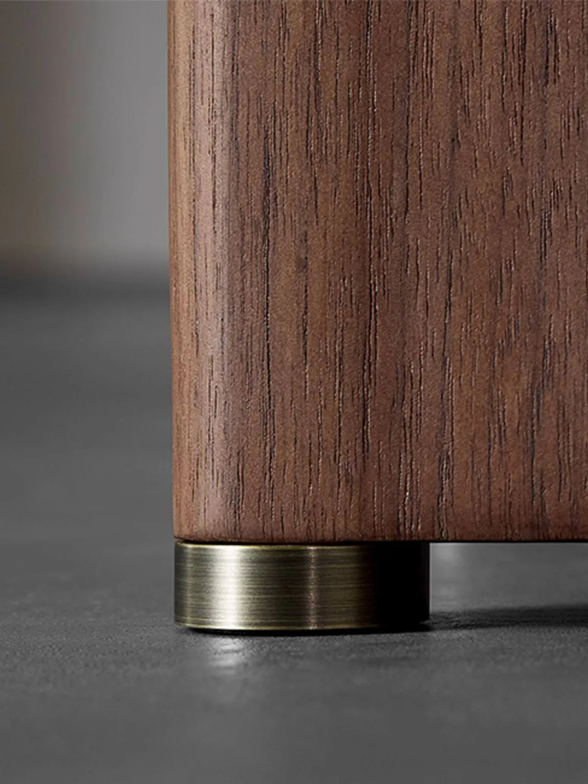 Detail of the Kurumi table's fluted walnut pedestal leg with a brushed brass metal ring inlay at the floor.

