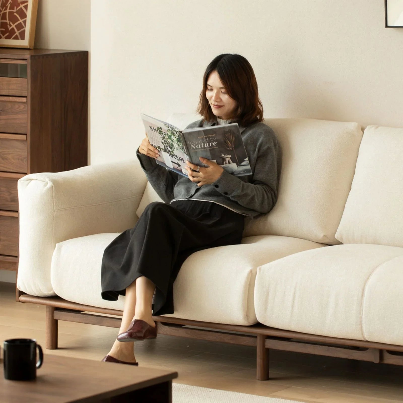 Woman reading magazine on cream fabric walnut wood sofa in cozy modern living room