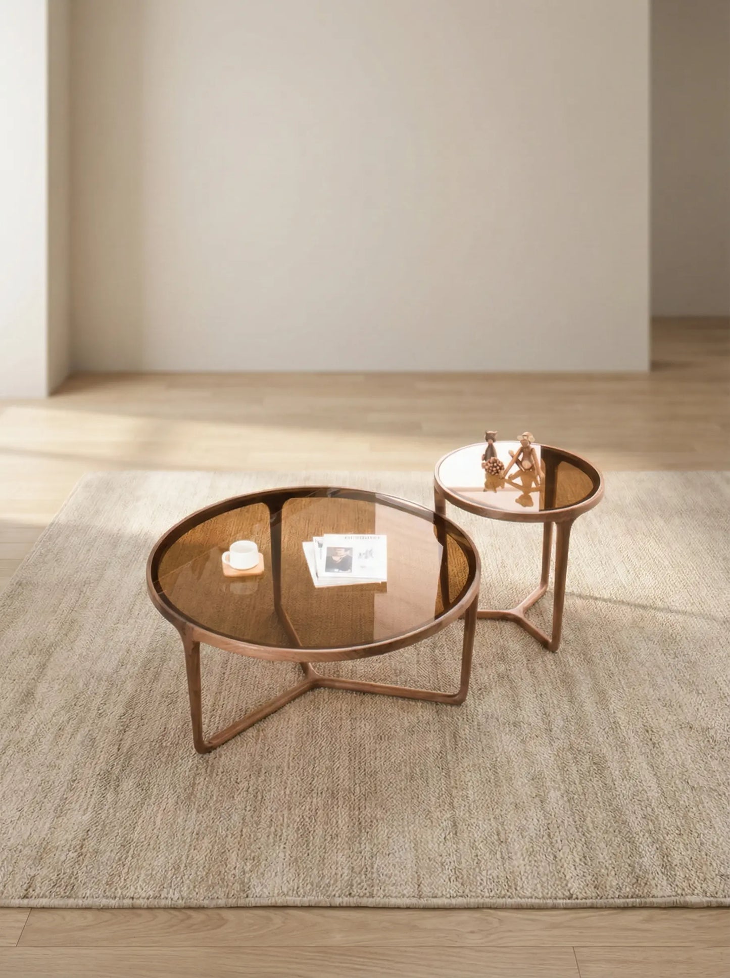 The Solstice nesting set placed next to a modern grey sectional sofa, providing a reference for scale and demonstrating the layered look of the two table heights.