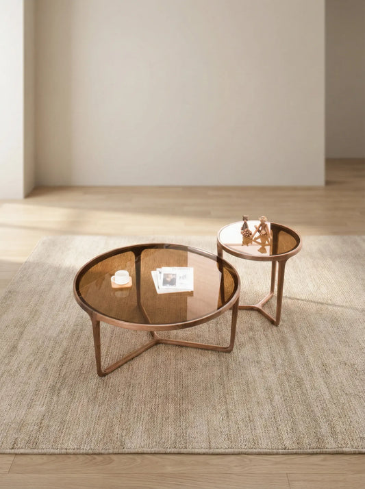 The Solstice nesting set placed next to a modern grey sectional sofa, providing a reference for scale and demonstrating the layered look of the two table heights.