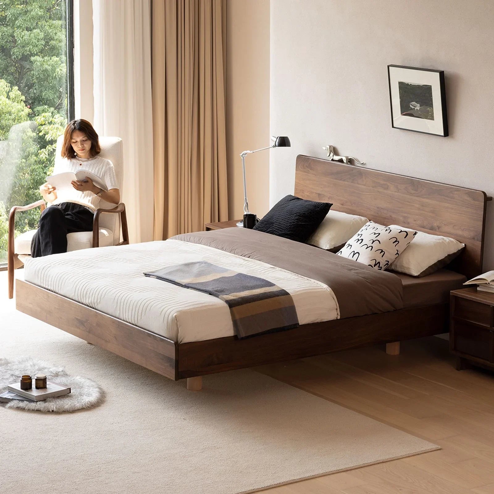 Mid-century modern bedroom with floating wooden bed, beige curtains, and woman reading in armchair
