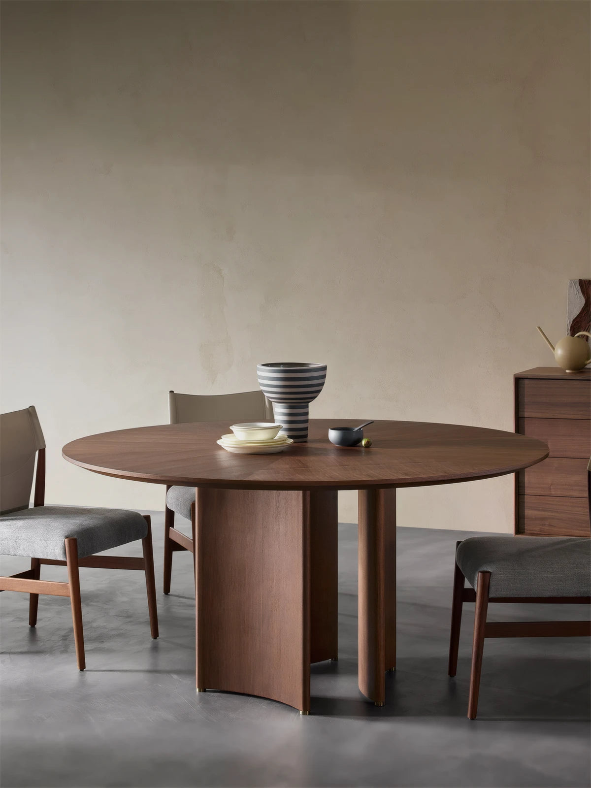 Round walnut dining table styled in a minimalist Japandi home with ceramic vase, linen napkins, and wishbone chairs.