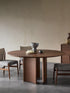 Round walnut dining table styled in a minimalist Japandi home with ceramic vase, linen napkins, and wishbone chairs.