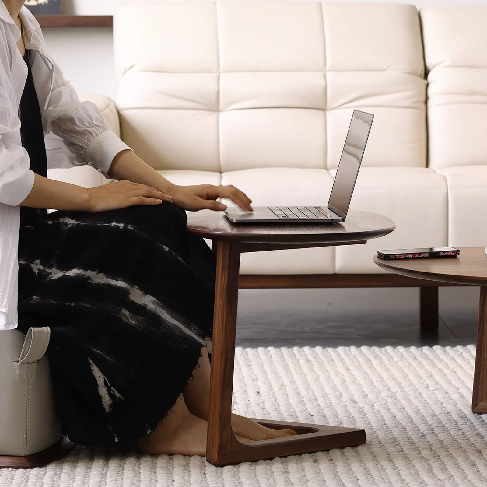 Mid-century modern round walnut side table with laptop, white sofa, and textured rug in living room