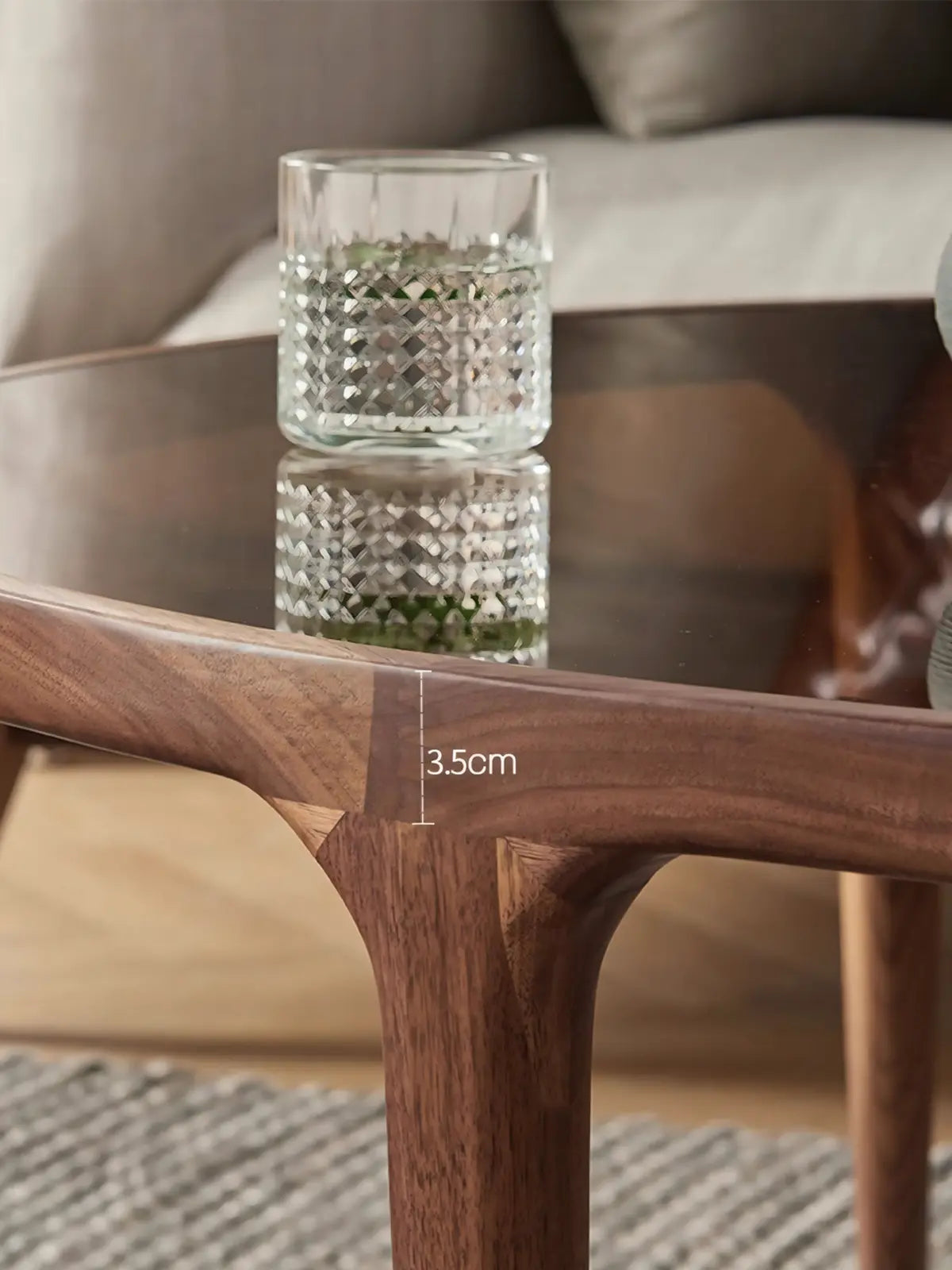 Close-up detail of the Solstice coffee table showing the seamless joinery of solid North American Black Walnut legs meeting the polished edge of the 10mm amber tempered glass top.