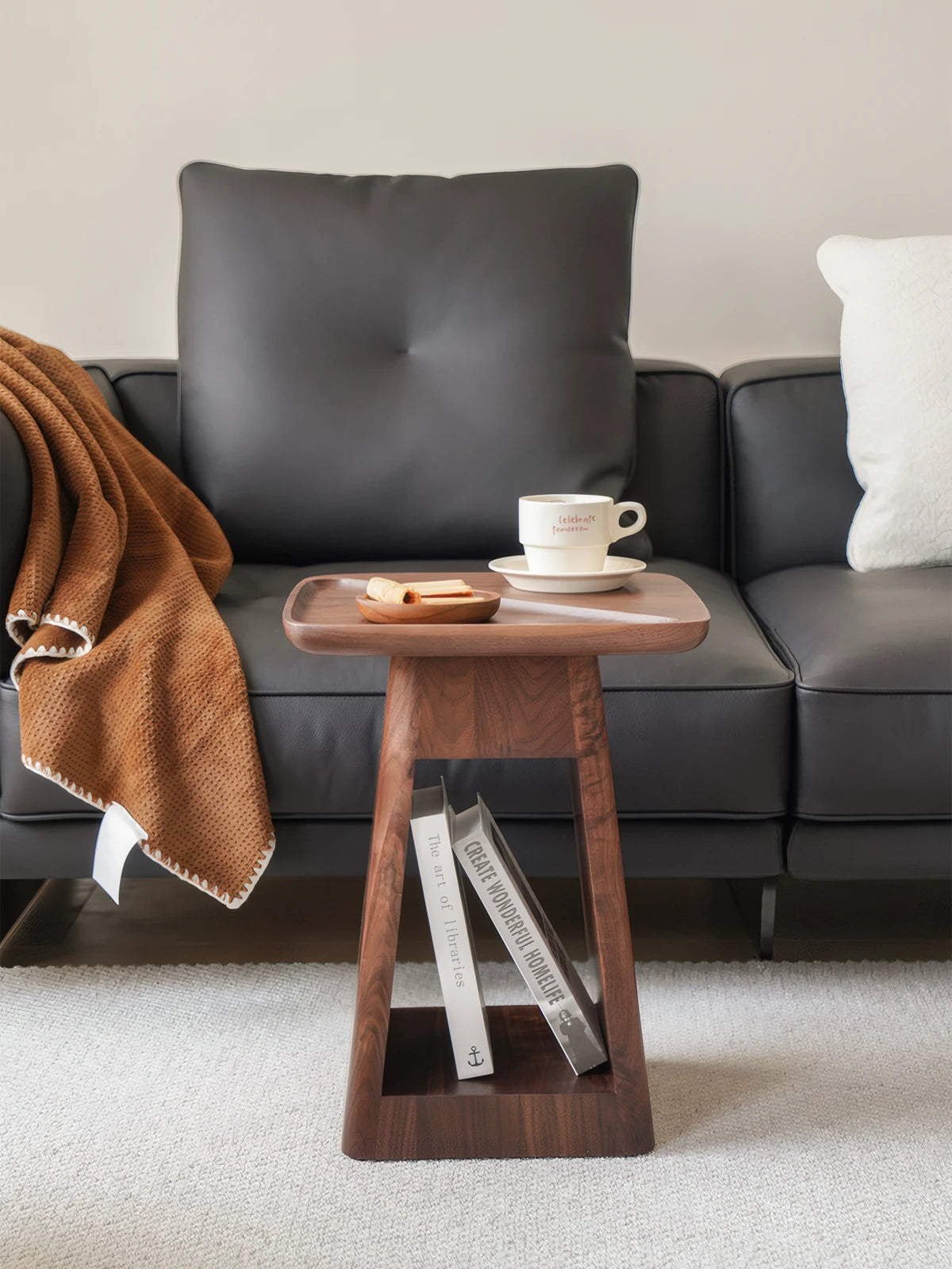 Front view of the Kurumi table showing the trapezoid solid wood legs and open storage shelf holding books.