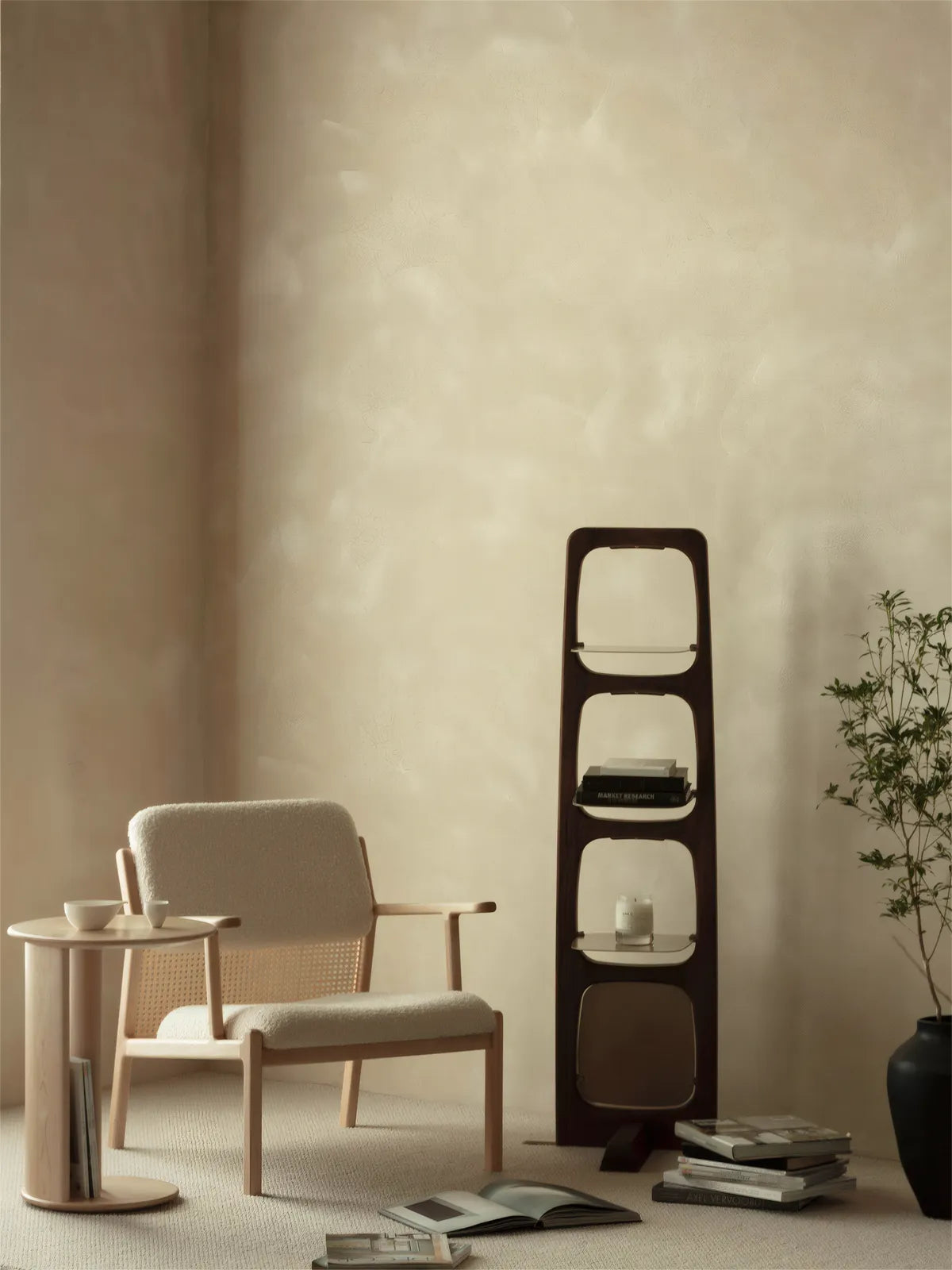 The mid-height walnut display shelf placed beside a boucle armchair, functioning as a side table and book display in a minimalist space.