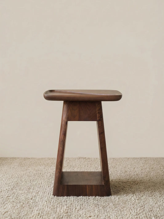 The Kurumi table standing alone against a neutral wall, highlighting its sculptural trapezoid silhouette and warm wood tones.