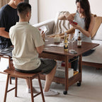 Three people playing cards around a wooden table with beer bottles and wine glasses in a cozy living room