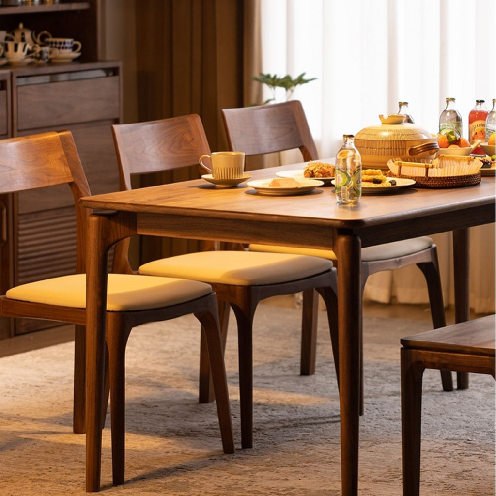 wooden dining table with upholstered chairs set with plates, cups, bottles, and food in modern dining room