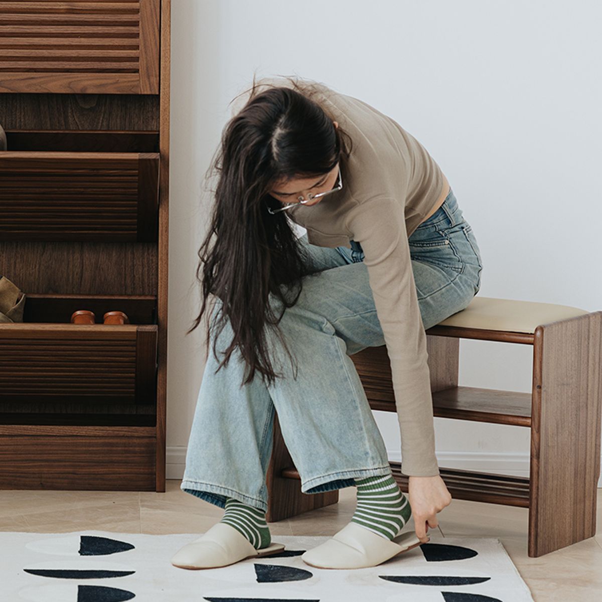 Woman wearing striped socks and white slippers sitting on walnut shoe bench in modern entryway