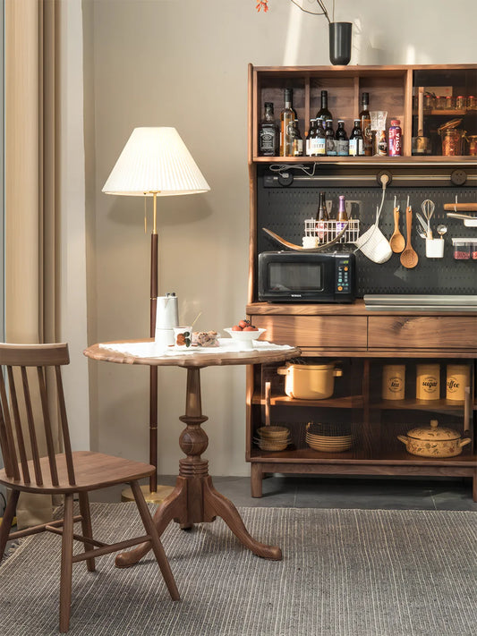 Wide shot of the round walnut pedestal table in a modern kitchen setting with ambient lighting and open shelving.