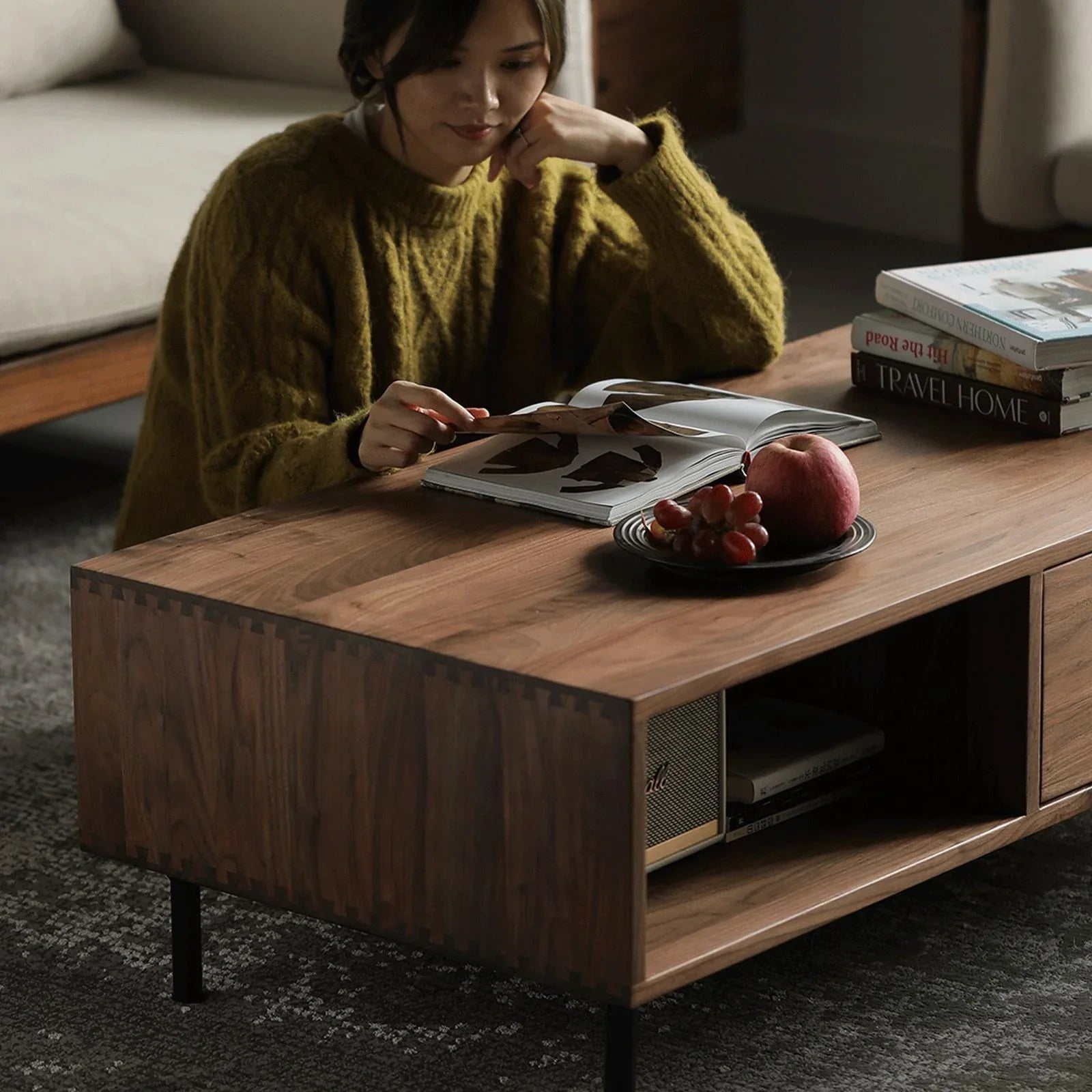 Modern minimalist wooden coffee table with storage shelves, woman reading book, fruit plate on table