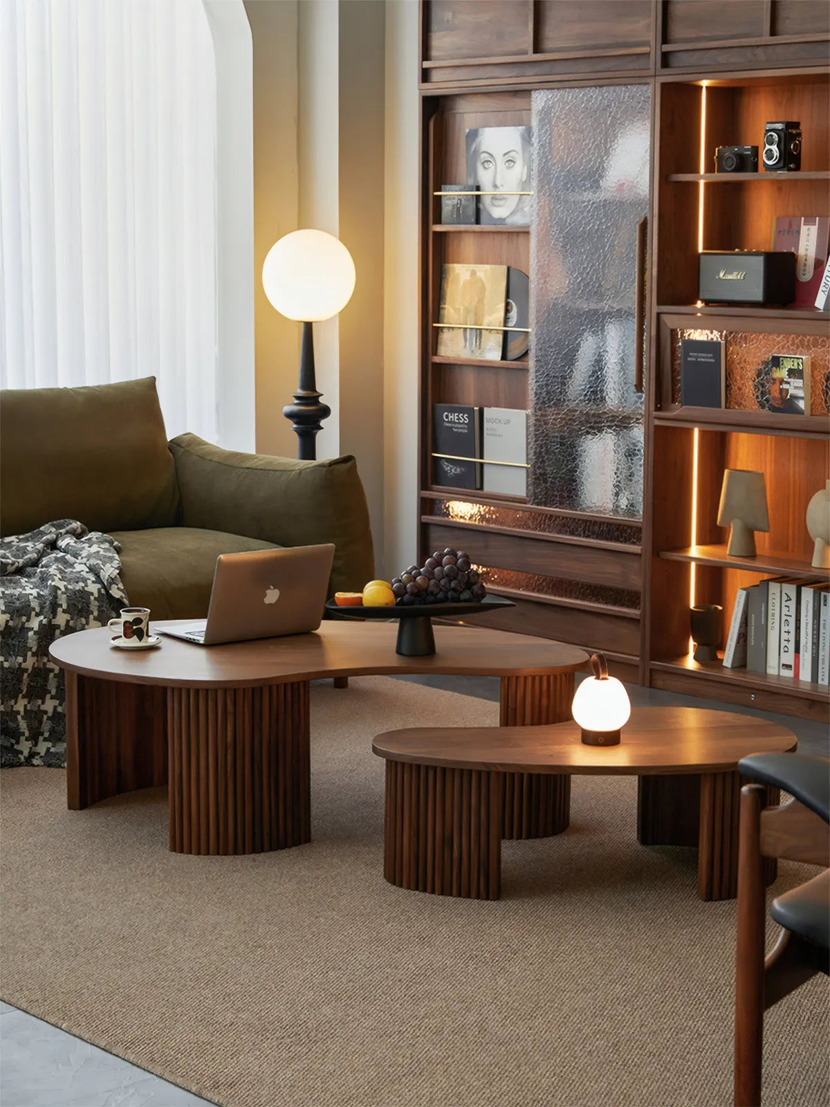 "Wide shot of Kurumi walnut cloud table styled in a modern living room with bookshelves and warm lighting."