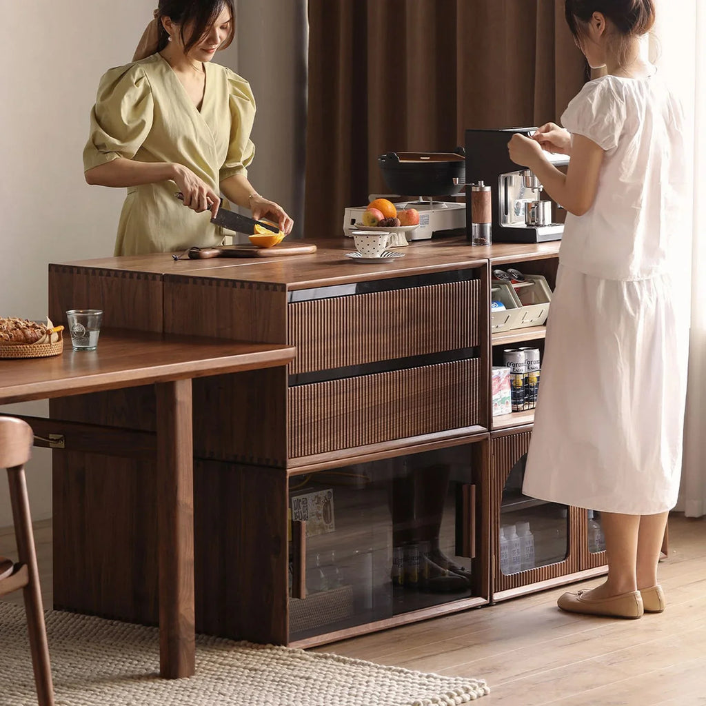 Two women using a modular walnut kitchen storage system with drawers and glass cabinets