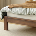 Close-up of natural walnut wood bed frame with carved details, white bedding and brown knit throw