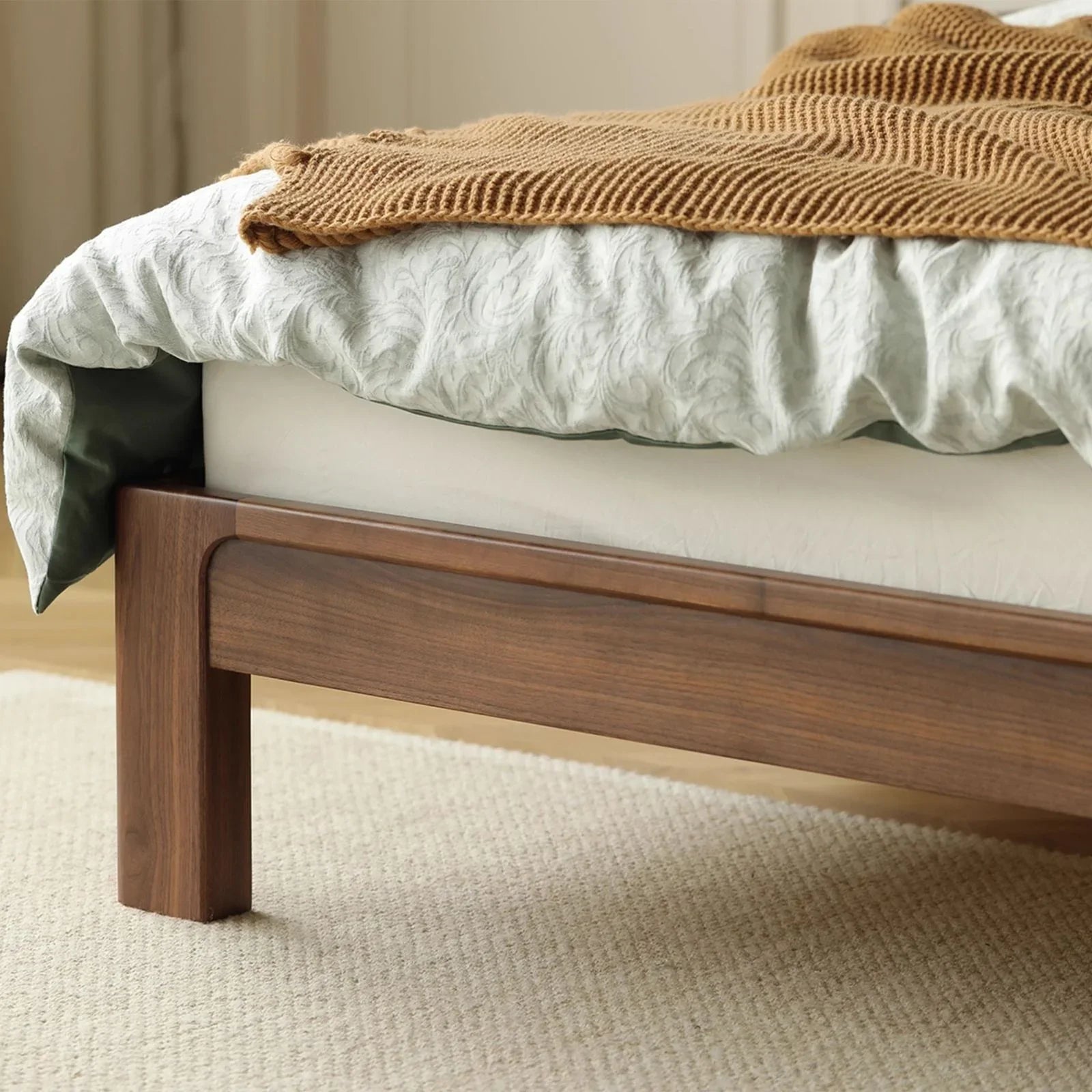 Close-up of natural walnut wood bed frame with carved details, white bedding and brown knit throw