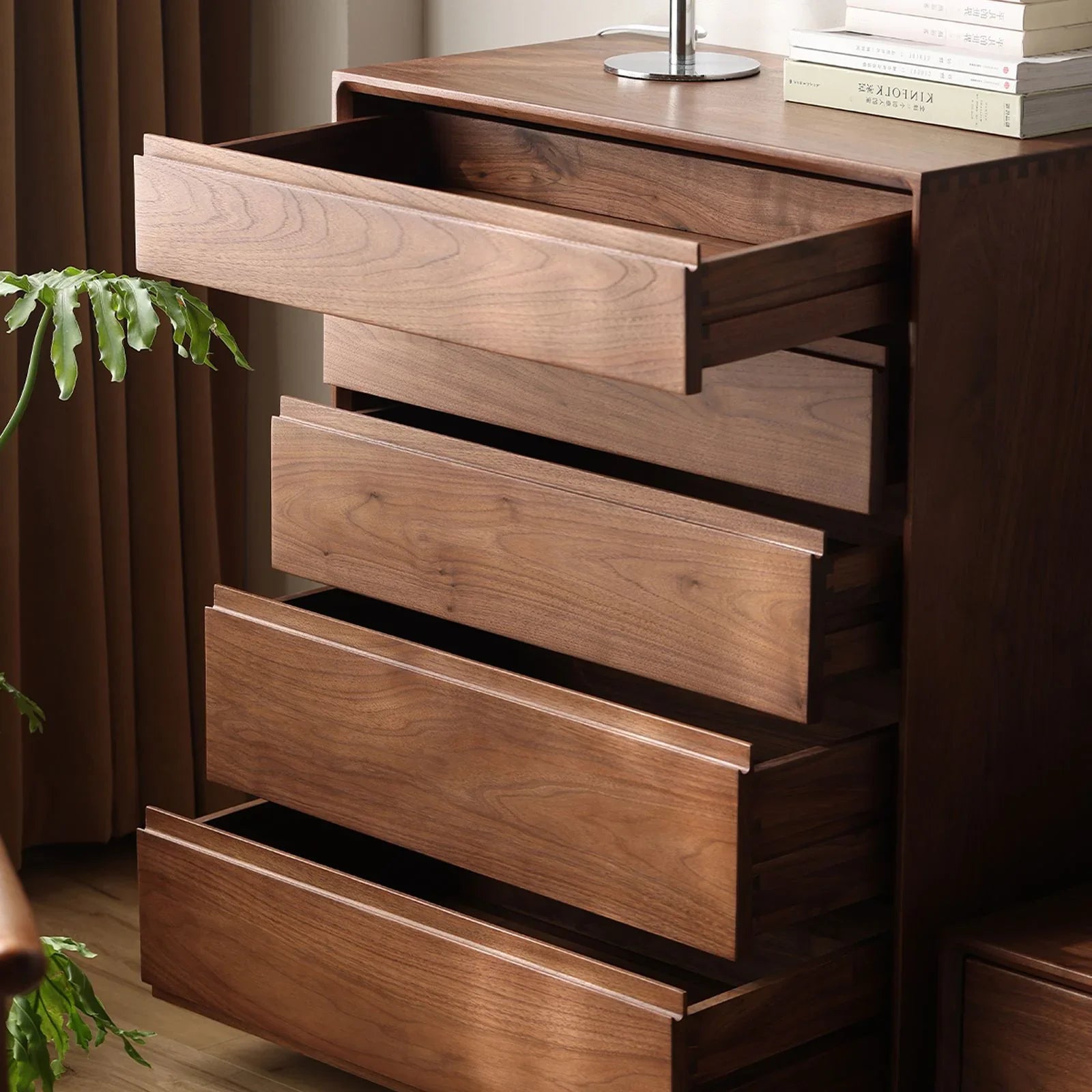 Open wooden drawers of a modern walnut bedroom dresser with books and a lamp on top