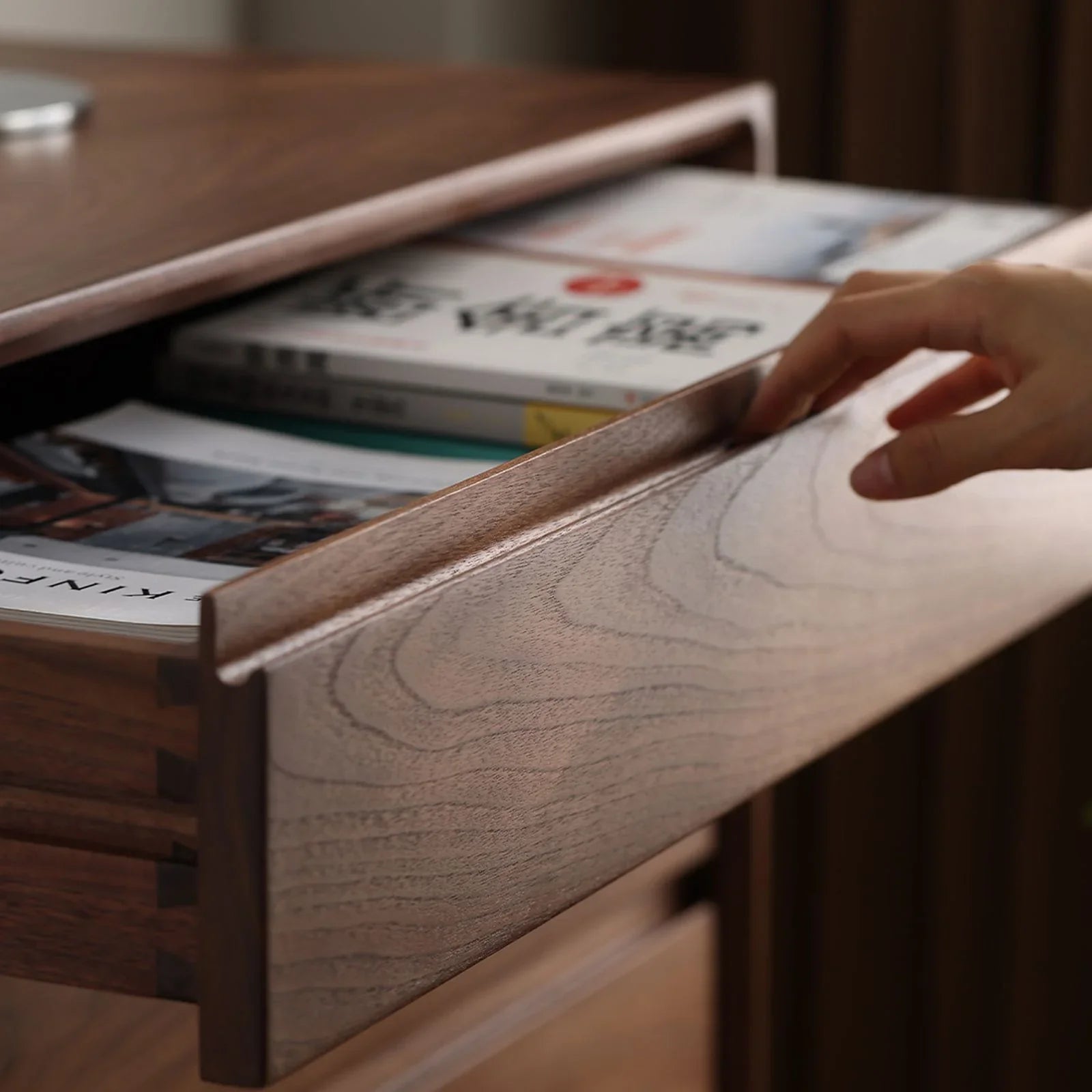 Hand opening a solid black walnut bedroom drawer with magazines inside, highlighting wood grain and storage