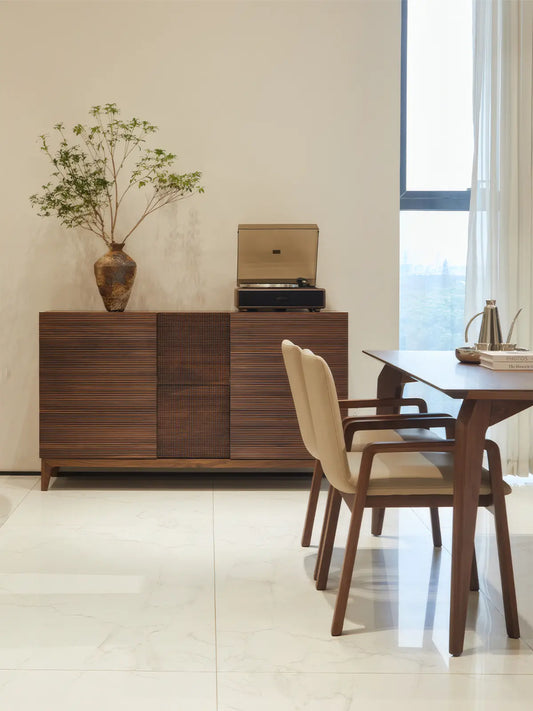 The Opus solid walnut sideboard styled as a dining room buffet, featuring a record player and floral arrangement, showcasing its mid-century modern aesthetic.