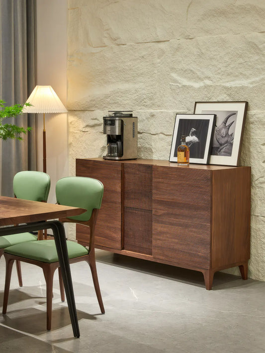 The Opus walnut buffet cabinet in a textured dining room setting with green chairs, functioning as a stylish coffee station and storage unit.