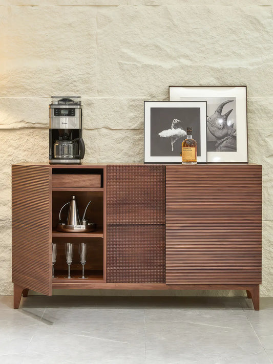 The Opus walnut sideboard with the left door open, revealing internal storage shelves, a drawer, and a wine glass rack used as a coffee or bar station.