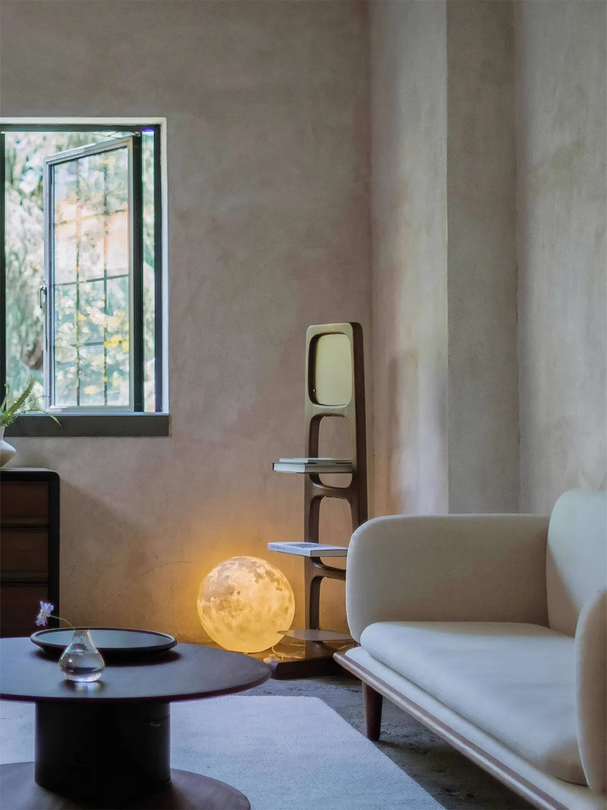 The Ocular walnut shelf styled next to a window in an organic modern living room, featuring a moon lamp on the bottom shelf.