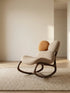 Side profile of The Cairn Rocker in Sandstone beige, showing the fluid wooden curves and ergonomic recline angle.
