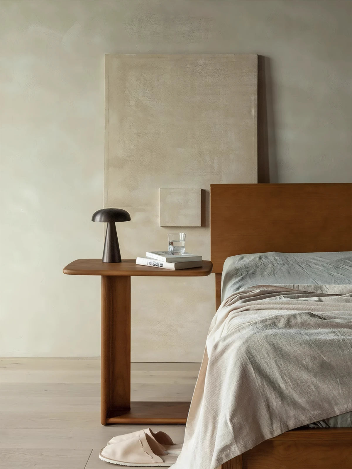 Walnut C-shaped end table next to a wooden headboard, holding a modern black mushroom lamp and books.
