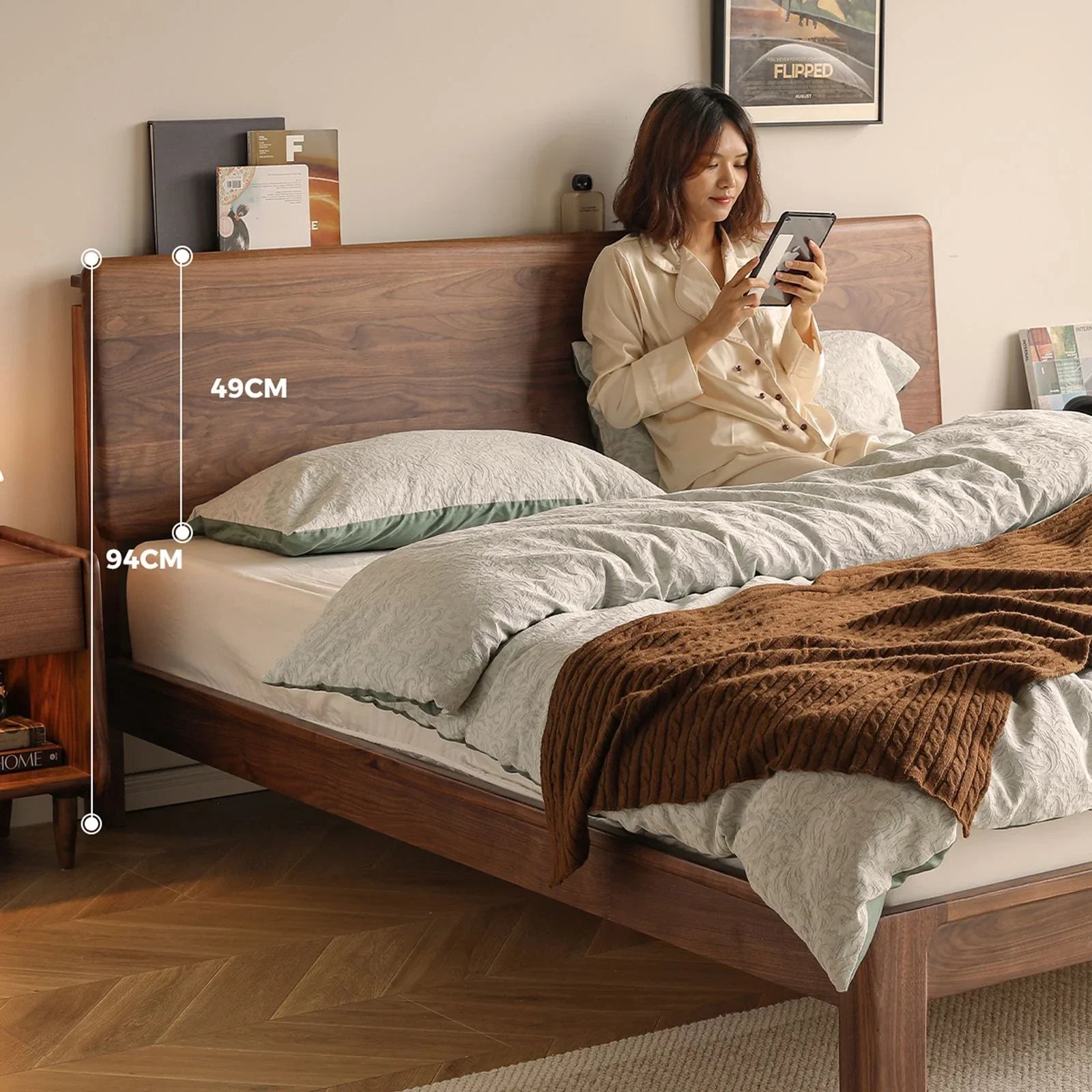Woman in pajamas using tablet on walnut wood bed with grey bedding and brown throw