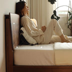 Woman in cream pajamas relaxing on wooden bed with cream bedding in cozy bedroom