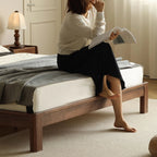 Woman reading on a mid-century modern walnut bed with gray striped blanket in cozy bedroom