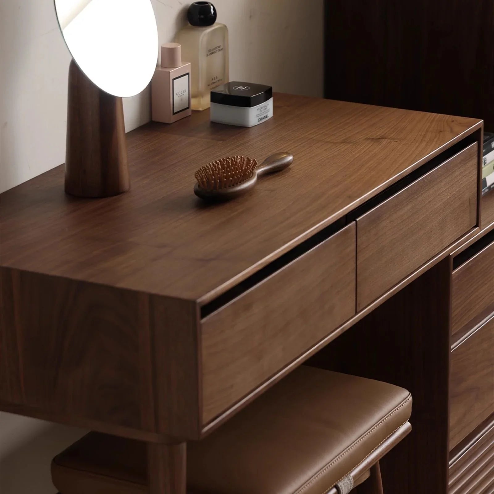 Modern walnut vanity setup with illuminated mirror, wooden hairbrush, luxury perfumes, and leather stool
