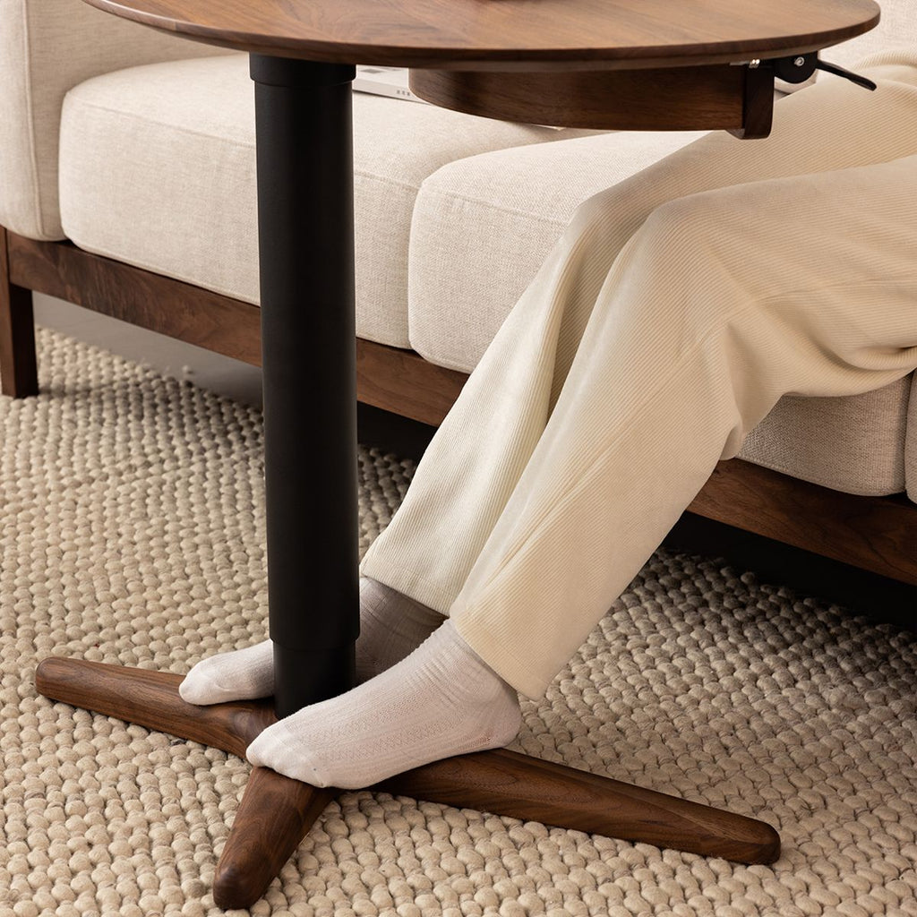 Person with white socks and beige pants using a wooden and black metal laptop side table next to beige sofa