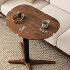 Wooden sofa side table with black metal pedestal base, beige couch, headphones and mug on textured rug