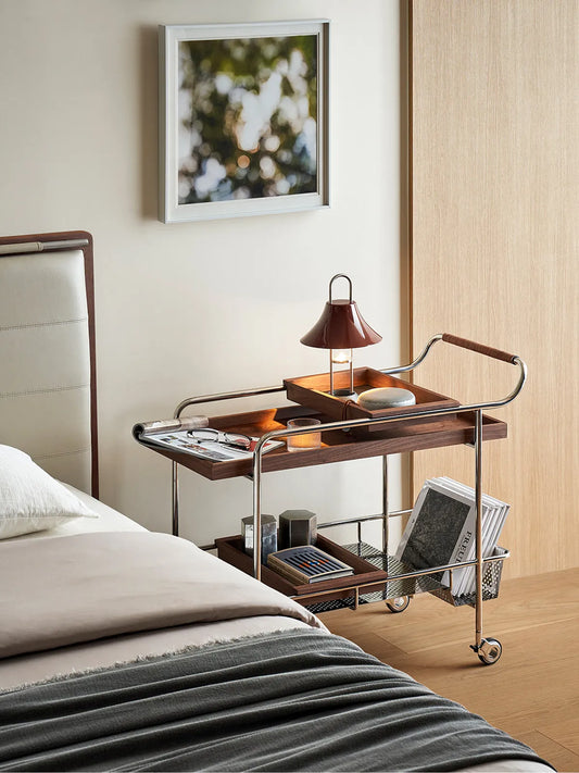 Walnutry bar cart styled as a nightstand in a bedroom, featuring a lamp and books on the walnut tray.