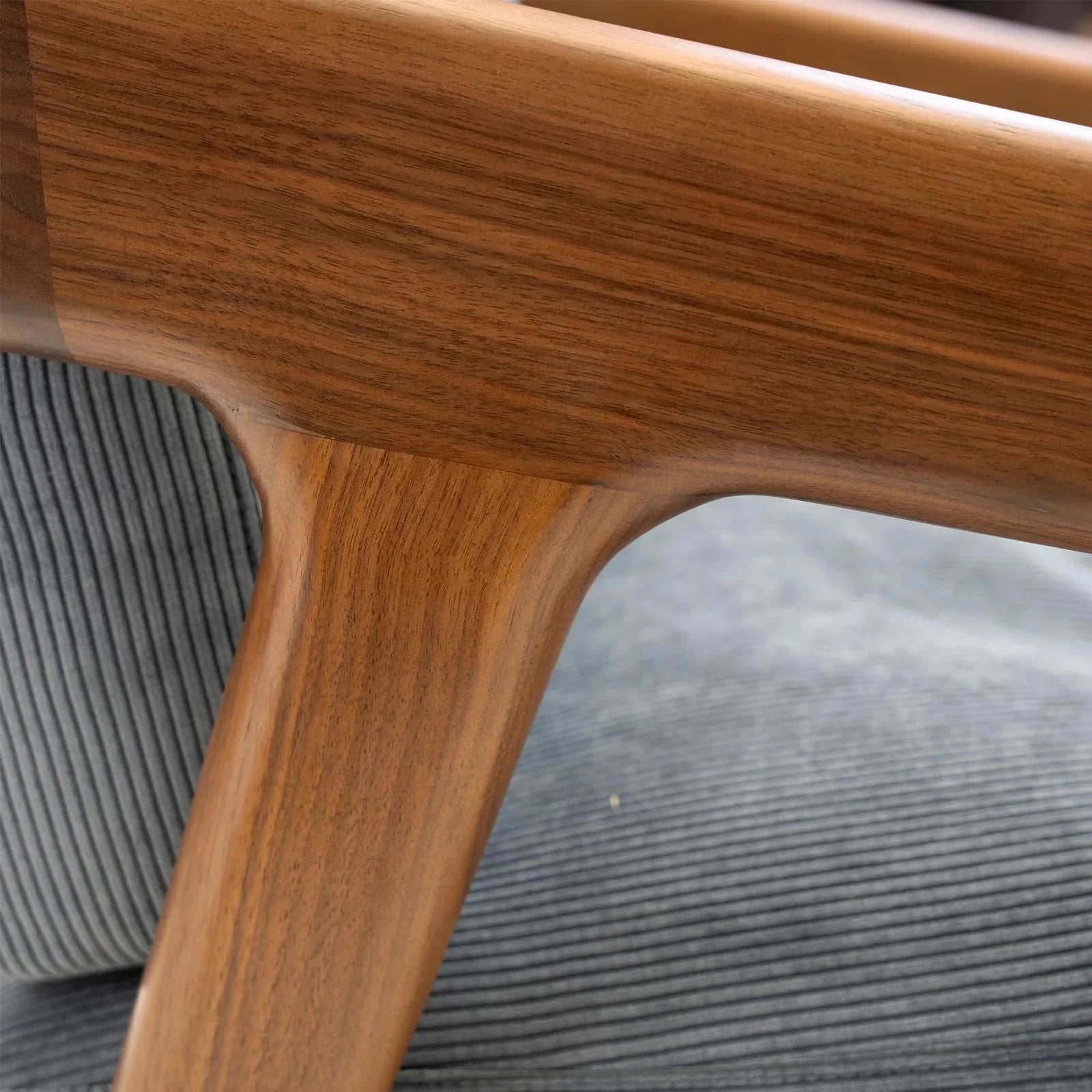 Close-up of Walnutry solid black walnut lounge chair armrest with textured gray fabric cushion