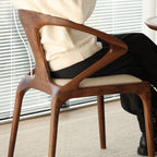 Solid walnut chair with unique geometric backrest and beige cushioned seat in indoor setting