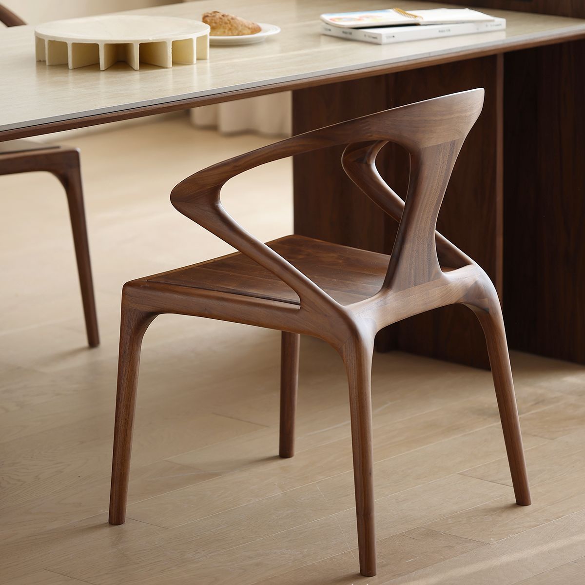 Solid walnut chair with sculptural backrest near light wood dining table in modern dining room