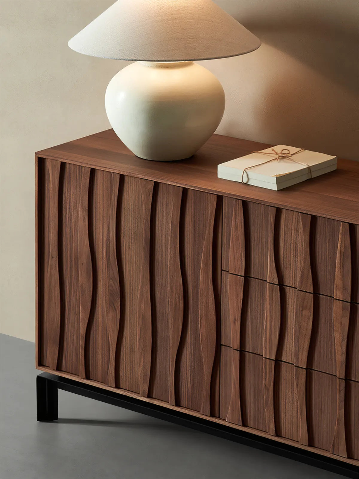 Top angle detail of solid walnut credenza showing wood grain texture, styled with a ceramic lamp and books, highlighting the smooth natural finish.