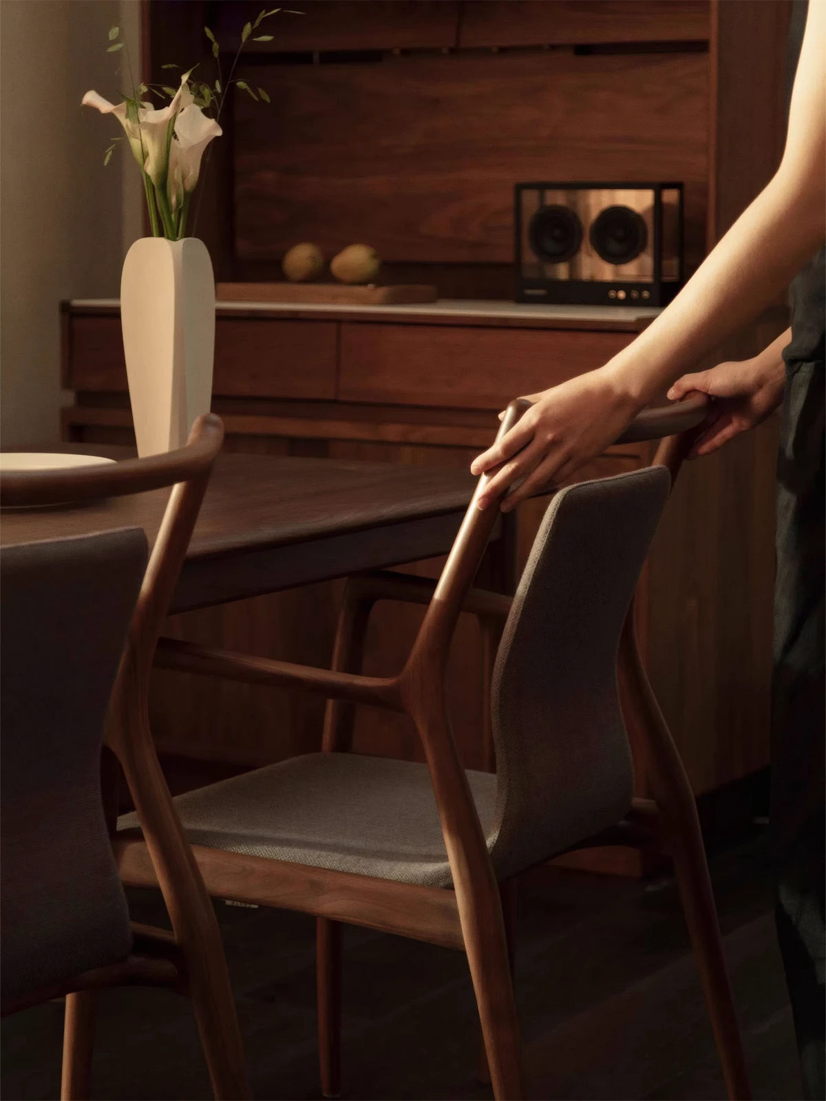 Close-up of a hand touching the smooth, curved backrest of a Walnutry solid walnut dining chair, highlighting the ergonomic design and wood texture.