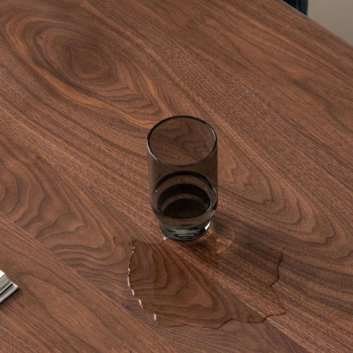 Close-up of solid walnut dining table surface with water spill and glass showcasing walnut wood grain